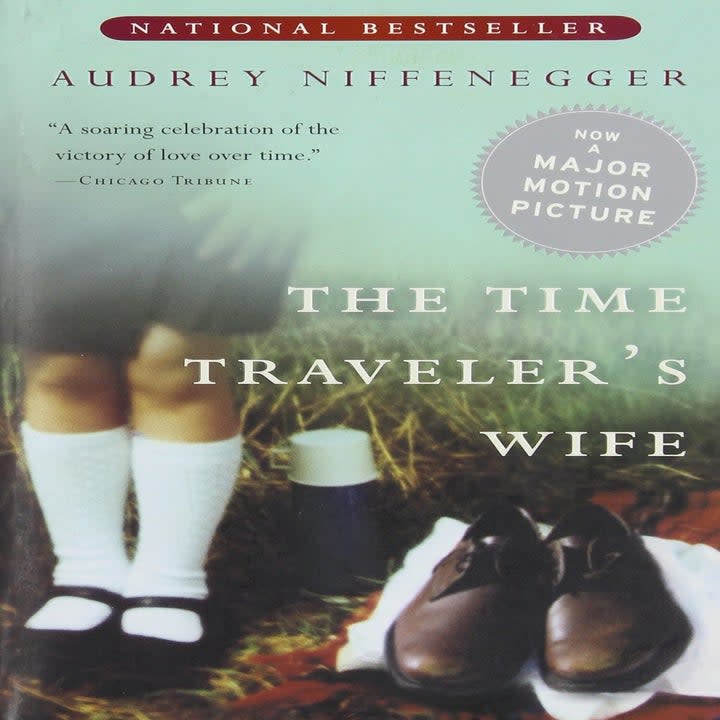 The cover of the novel which shows a close up of someone's legs next to a pair of men's shoes and clothes in the grass