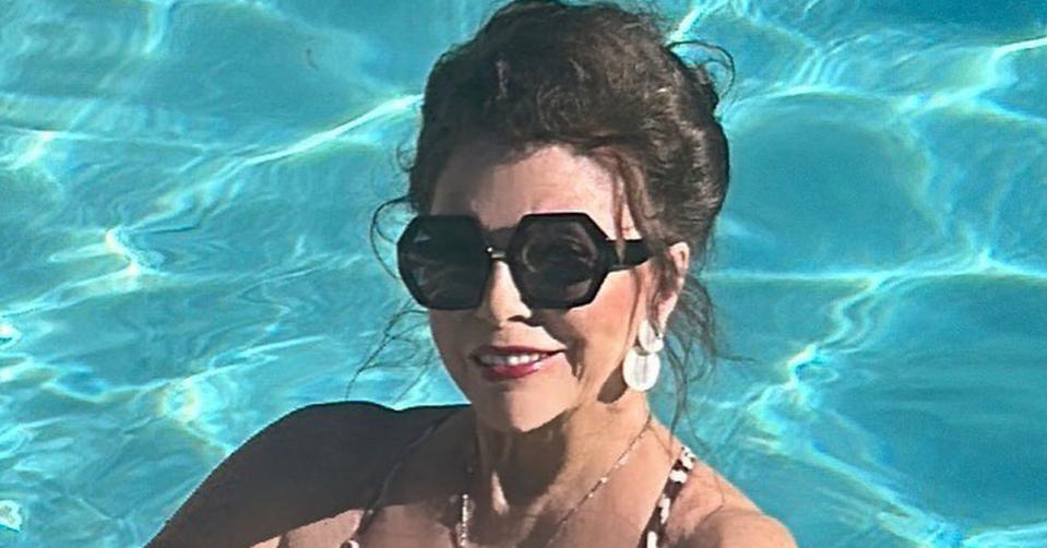 Joan Collins wearing large black sunglasses while standing in a pool