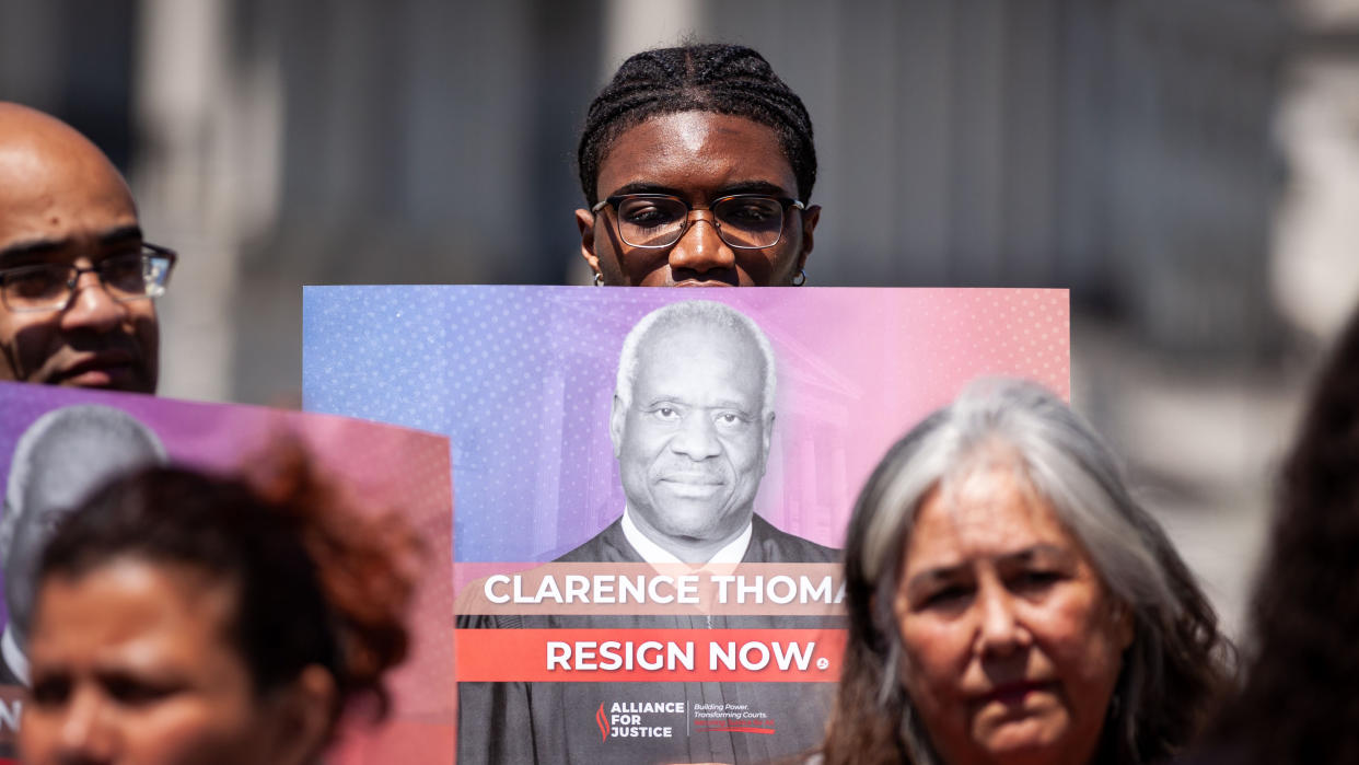 A young activist holds up a poster of Supreme Court Justice Clarence Thomas saying: Clarence Thomas, Resign Now, Alliance for Justice.