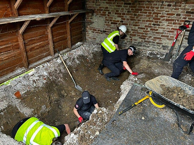 Four men digging a hole in the floor of a barn