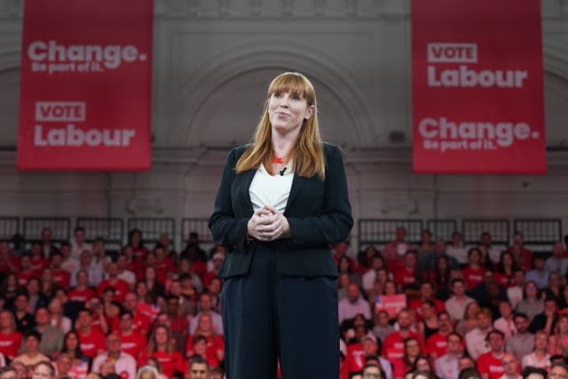 Angela Rayner stands with her hands together in front of supporters and 'Vote Labour' banners