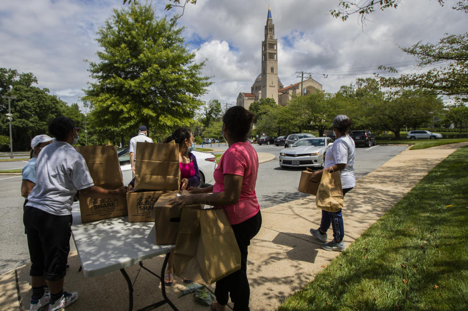 Area residents without a car wait in line for a ride after picking up food items distributed to families affected by the coronavirus pandemic at the Basilica of the National Shrine of the Immaculate Conception Friday, July 10, 2020, in Washington. The food distribution was hosted by the Catholic Charities of the Archdiocese of Washington. (AP Photo/Manuel Balce Ceneta)