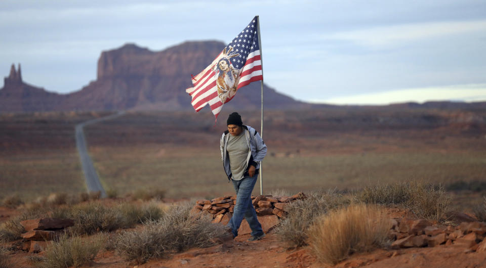 FILE - In this Thursday, Oct. 25, 2018, photo, Brandon Nez displays his flag at near his jewelry stand in Monument Valley, Utah, where tourists stand the highway to recreate a famous running scene from the movie "Forest Gump". As Native American tribes around the country fight for increased access to the ballot box, Navajo voters in one Utah county could tip the balance of power in the first general election since a federal judge ordered overturned their voting districts as illegally drawn to minimize native voices. Native Americans weren't granted U.S. citizenship until 1924, and even then some states prohibited them from voting for decades if they lived on reservations or couldn't pass an English literacy test. (AP Photo/Rick Bowmer, File)