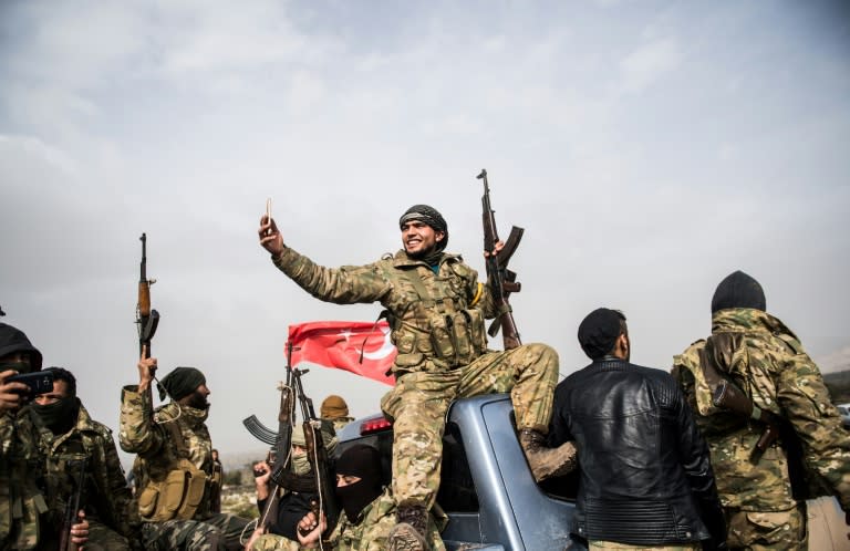 A Turkey-backed Syrian rebel fighter takes a selfie in front of Turkish troops near the village of Hassa on the Syrian border