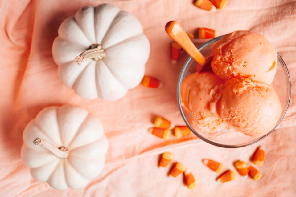 orange sherbet, mini white pumpkins, candy corn candies styled on a peach textured background