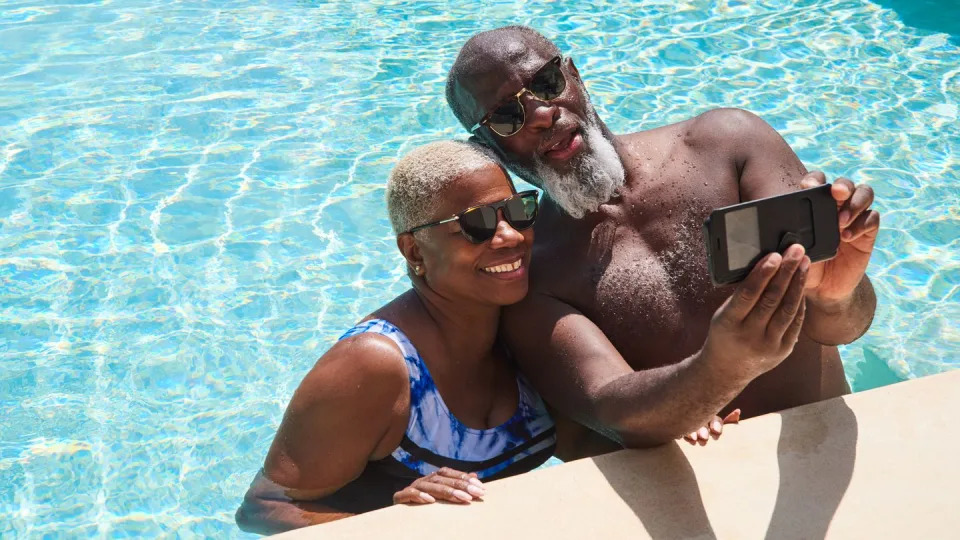 a mature couple huddle at a swimming pools edge and take a photo of themselves on vacation