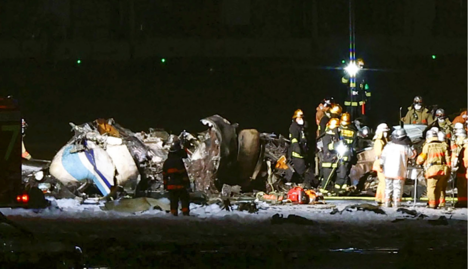 Firefighters inspect a part of the Japanese coast guard aircraft on the runway of Haneda airport  (AP)