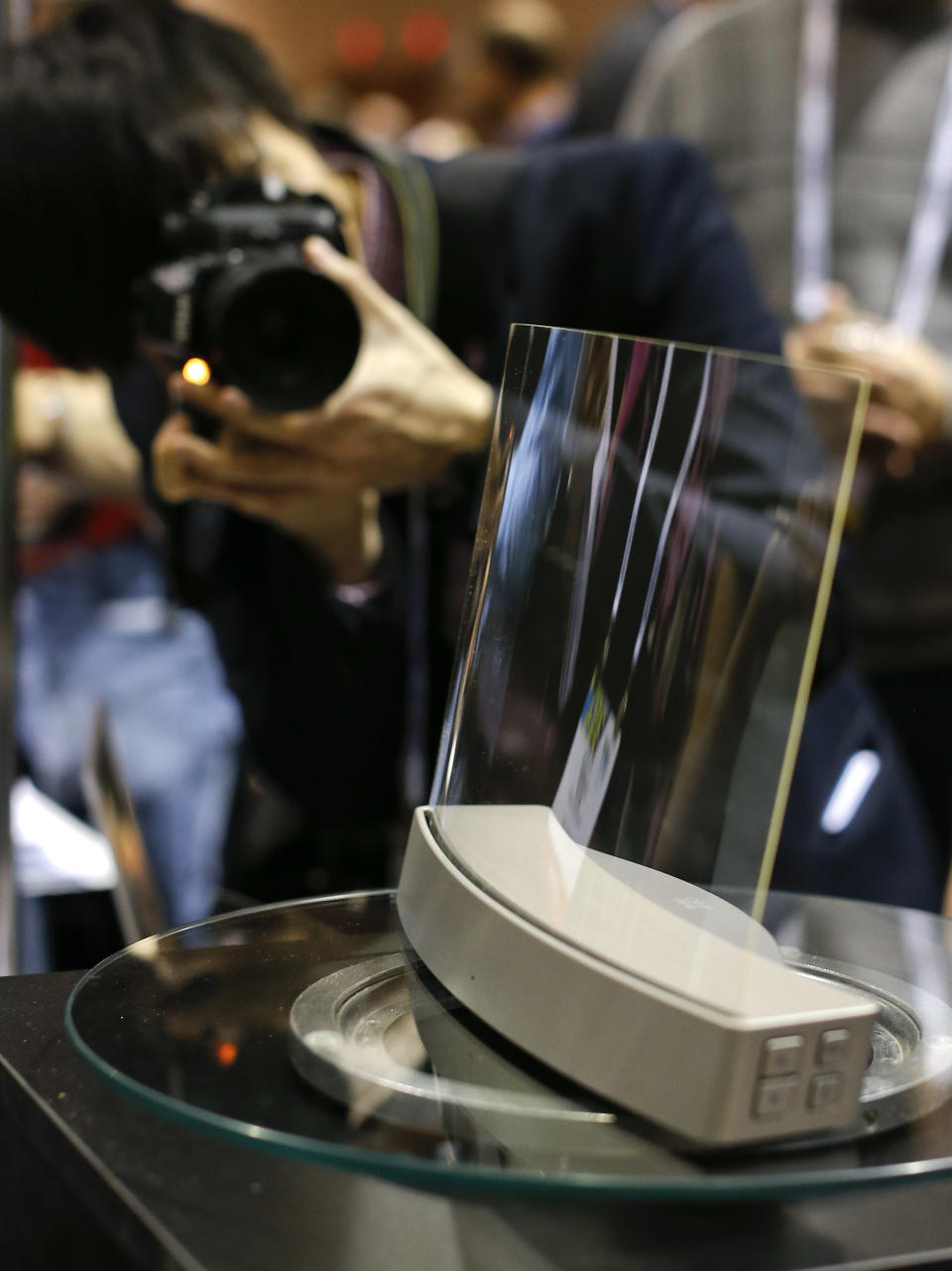 Members of the media photograph a glass speaker called Clio during the International Consumer Electronics Show, Sunday, Jan. 5, 2014, in Las Vegas. The speaker, produced by ClearView Audio uses a single piece of curved millimeter-thick acrylic glass that sits on a dock which vibrates it in a finely tuned way so that it can play music. It works with Bluetooth streaming and with a 3.5 millimeter jack. (AP Photo/Julie Jacobson)