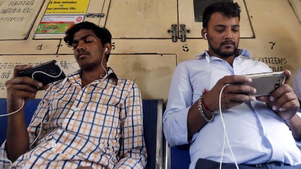 Two Indian men watch videos on their mobile phones as they travel in a suburban train in Mumbai