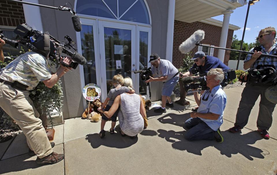 Sarah Madison (L) and her son Beckett, 3, are surrounded by media as they look at stuffed animals placed at the doorway of the River Bluff Dental clinic in protest against the killing of a famous lion in Zimbabwe, in Bloomington, Minnesota July 29, 2015. (REUTERS/Eric Miller)