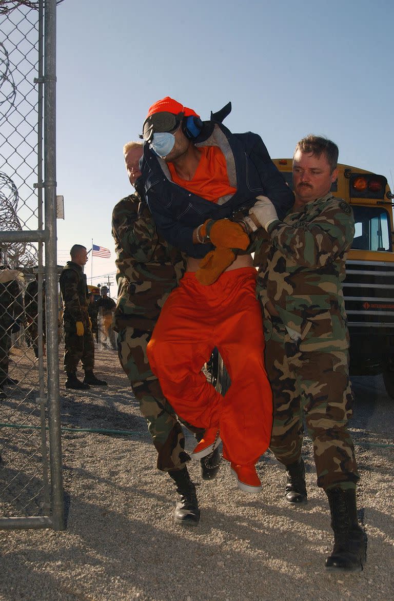  En una imagen proporcionada por la Marina, la policía militar levanta a un prisionero sin nombre de un autobús a un lugar de procesamiento en el centro de detención Camp X-Ray, en la Base Naval de Guantánamo en Cuba el 21 de enero de 2002.