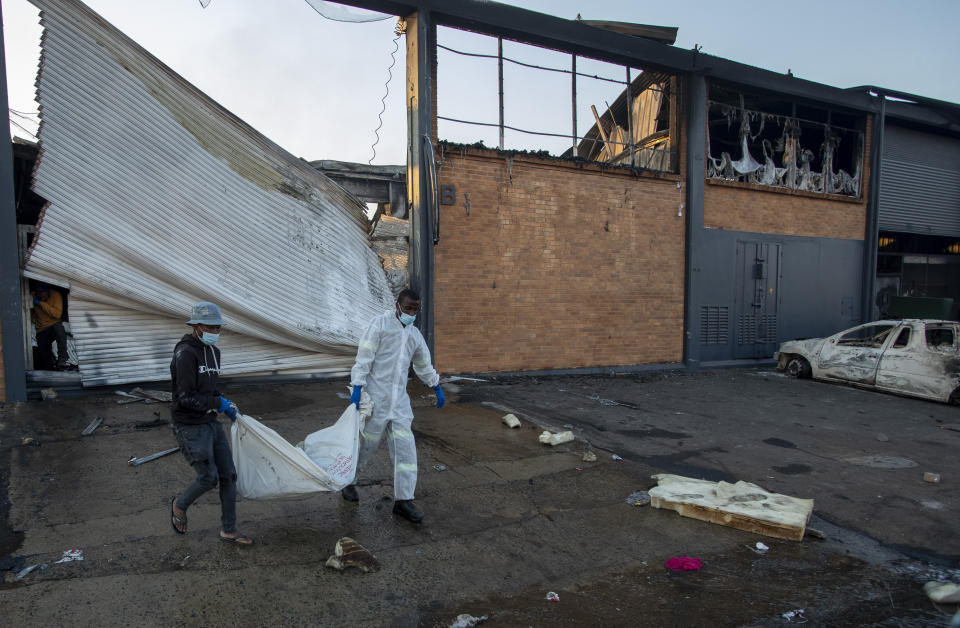 A family member assists a police officer to carry a body of a man who was found inside a burned shop, in Johannesburg, South Africa, Sunday, July 11, 2021. Protests have spread from the KwaZulu Natal province to Johannesburg against the imprisonment of former South African President Jacob Zuma who was imprisoned last week for contempt of court. (AP Photo/Themba Hadebe)