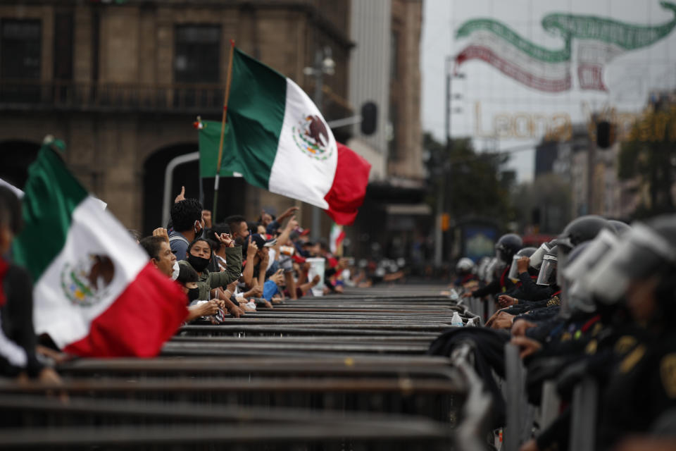 Some participants in a protest marking the sixth anniversary of the forced disappearance of 43 teachers' college students shout over a barricade and a line of police toward unrelated protesters camping out in Mexico City's main square to call for the renunciation of the president, Saturday, Sept. 26, 2020. (AP Photo/Rebecca Blackwell)