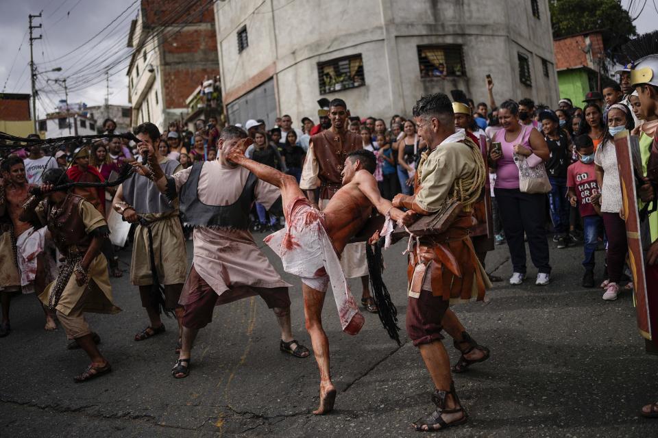 Un feligrés disfrazado de soldado romano (izquierda) azota a un penitente que desempeña el papel de uno de los dos ladrones sentenciados a ser crucificados a un costado de Jesucristo, durante la interpretación del Via Crucis el viernes 15 de abril de 2022, en el vecindario de Petare, en Caracas, Venezuela. (AP Foto/Matías Delacroix)