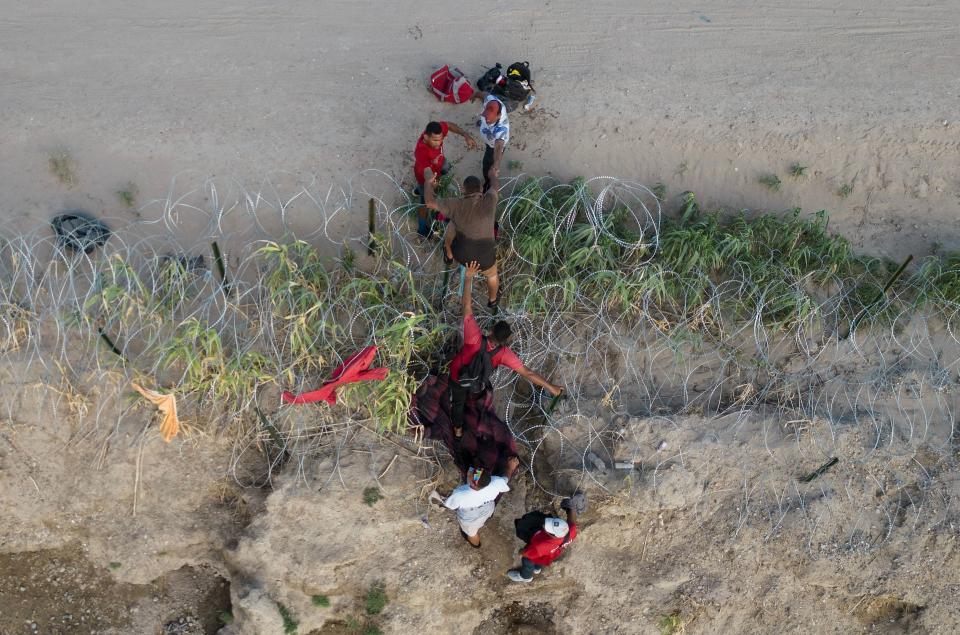 A group of migrants climb over razor wire as they cross the Rio Grande river at the US-Mexico border to Eagle Pass, Texas.