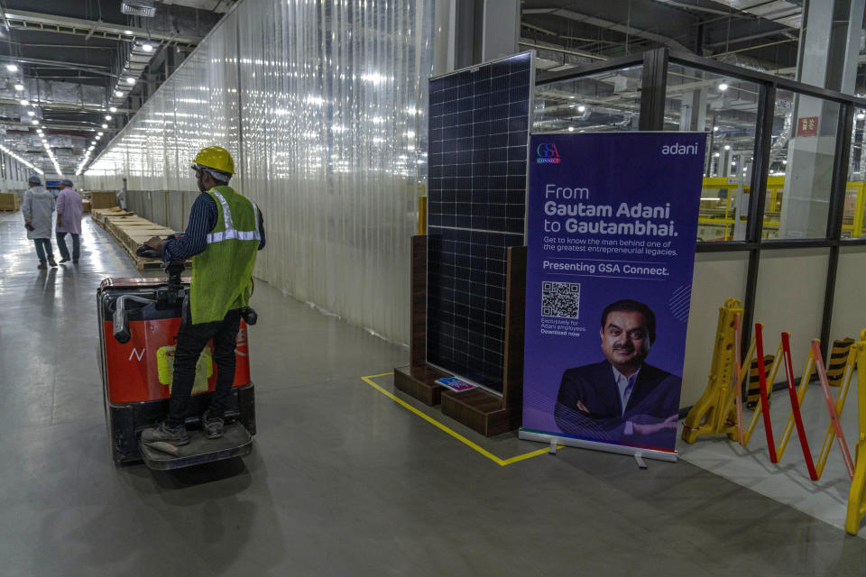 A load lifter operator wheels past a solar panel display alongside an image of Gautam Adani inside the Adani-owned Mundra Solar Techno-Park Private Limited, in the port town of Mundra in Western India's Gujarat state, India, Wednesday, Sept. 20, 2023. It's one of the few locations in India where most solar energy components are made from scratch. (AP Photo/Rafiq Maqbool)