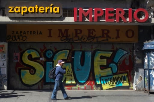 A man walks past a boarded up shoe store in valparaiso with graffiti that reads "Keep fighting!"