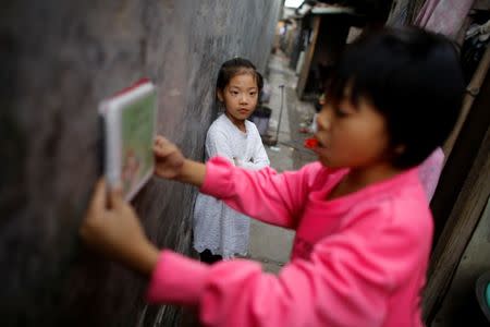 A neighbour child listens to Feng Aobin, the 10-year-old granddaughter of migrant worker Wang Qin, as she reads outside their home in a cluster of migrant homes at the outskirts of Beijing, China October 1, 2017. REUTERS/Thomas Peter