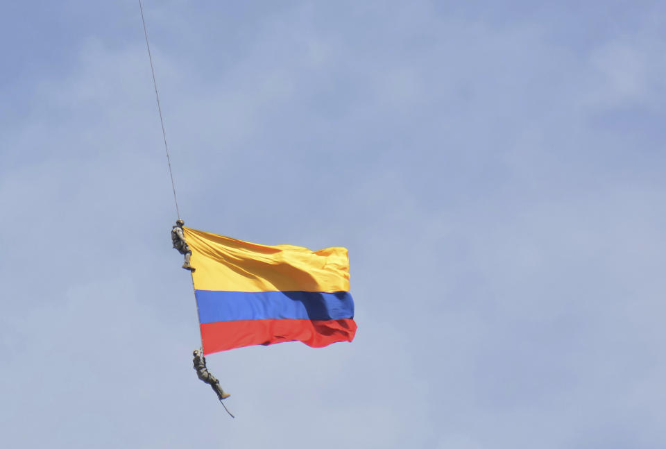Two members of Colombia´s air force hang from a cable under a helicopter flying a Colombian flag, before plunging to their deaths when the cable snapped during the mid-air stunt at the Medellin Flower Fair in Medellin, Colombia, Sunday, Aug. 11, 2019. (AP Photo/Luis Benavides)