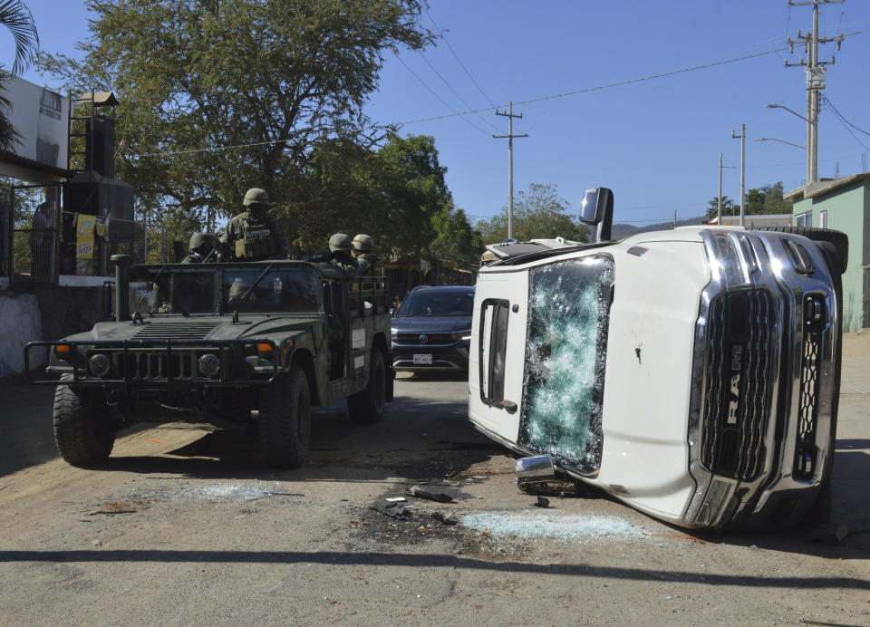 Army soldiers drive past a destroyed vehicle on the streets of Jesus Maria, Mexico, on Saturday, Jan. 7, 2023, the small town where Ovidio Guzman was detained earlier in the week. Thursday's government operation to detain Ovidio, the son of imprisoned drug lord Joaquin 