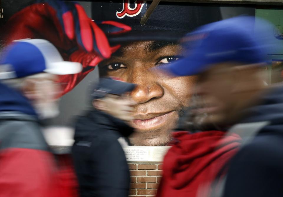 FILE - In this Oct. 1, 2016, file photo, fans at walk past a photograph of Boston Red Sox's David Ortiz before a baseball game against the Toronto Blue Jays at Fenway Park in Boston. Ortiz was back in Boston for medical care after authorities said the former Red Sox slugger affectionately known as Big Papi was ambushed by a gunman at a bar in his native Dominican Republic. A plane carrying the 43-year-old retired athlete landed Monday night, June 10, 2019, after a flight from the Dominican Republic, the team said. (AP Photo/Michael Dwyer, File)