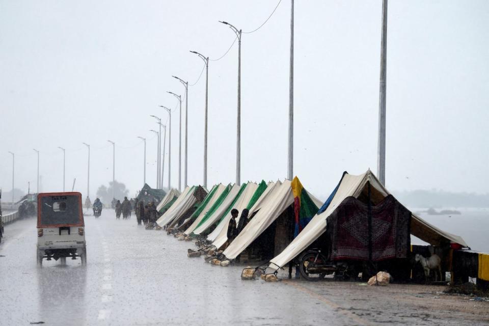 An auto-rickshaw drives past temporary tents of people who fled their flood-hit homes set along a road in Sukkur, Sindh province, on 27 August, 2022 (AFP via Getty Images)