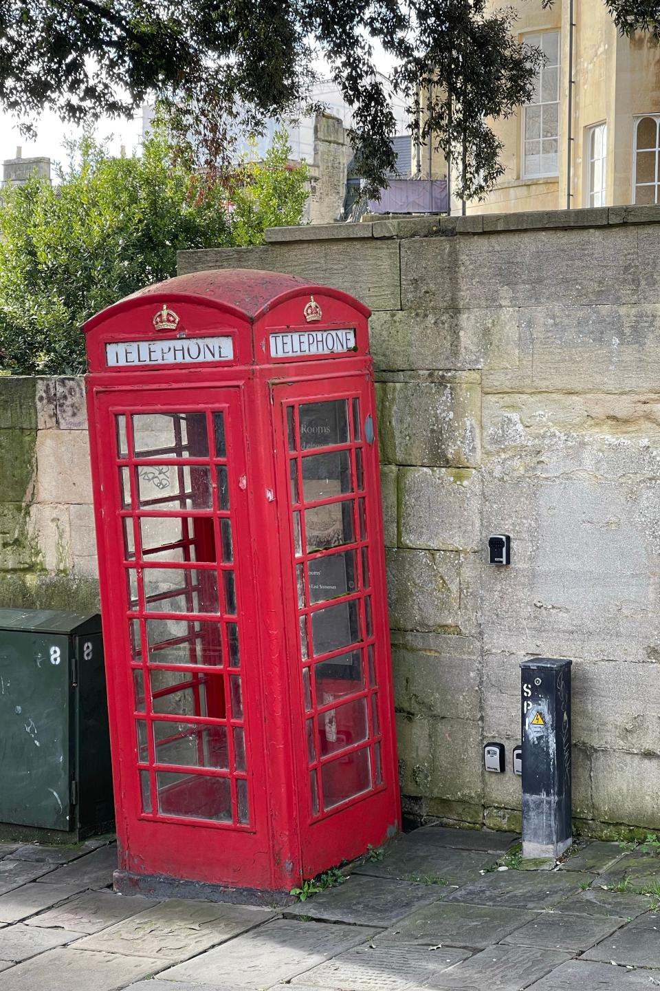 Two classic red British telephone booths stand side by side against a stone wall in an outdoor setting