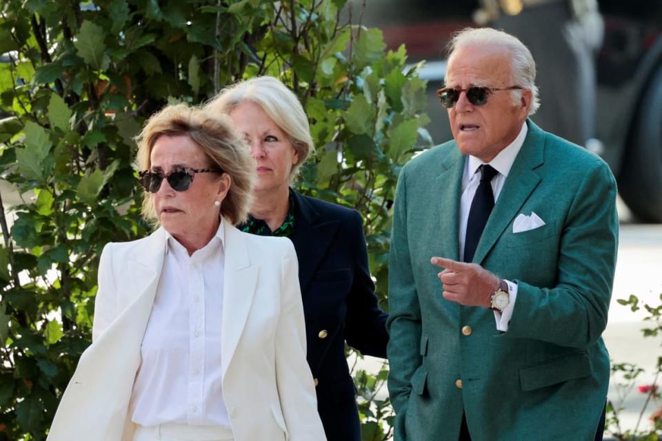 Valerie Biden Owens in white and wearings sunglasses in front of her brother James who is wearing a double-breasted green blazer