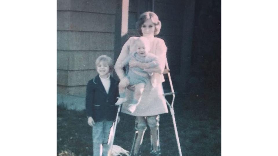 A woman on crutches carrying a baby while standing with a young boy