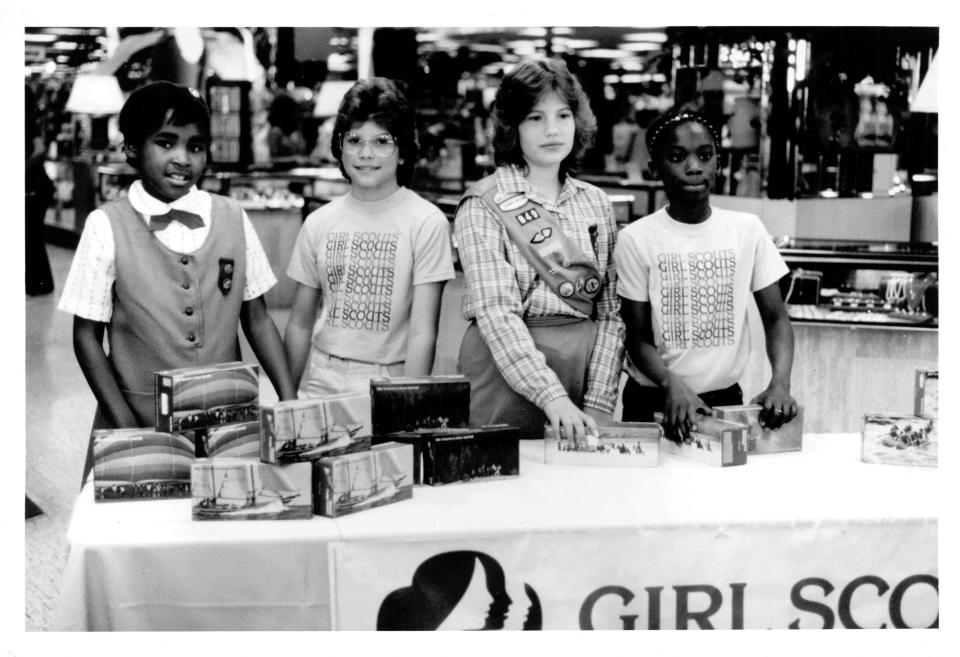 Three Girl Scout Brownies and one Cadette sell cookies in a local mall.