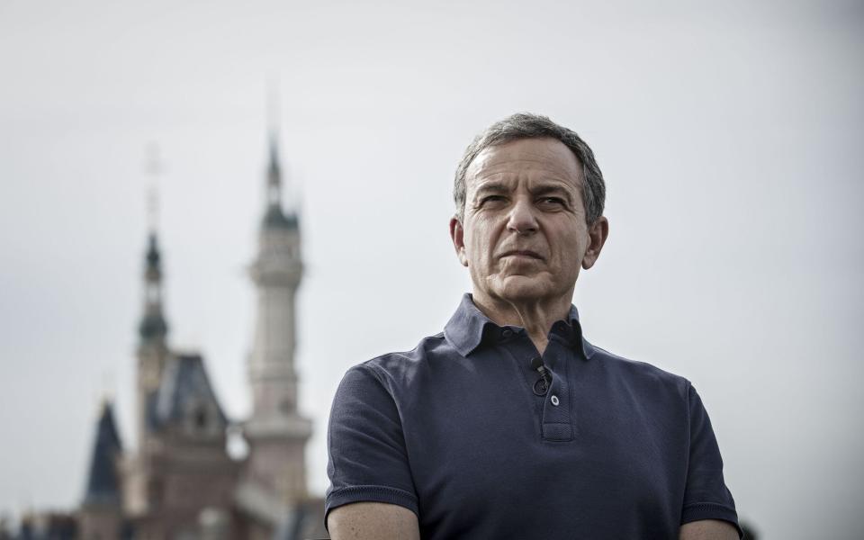 Bob Iger, a strongly-built white man wearing a navy blue polo shirt, with steel-grey hair and a deeply lined face, twists up the corner of his mouth in a dour expression as he takes questions in front of the fairytale spires of Disneyland Shanghai. - Qilau Shen/Bloomberg