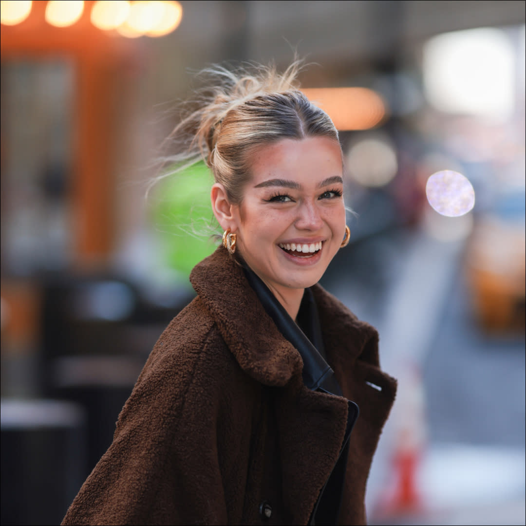  Millane Friesen is wearing a blue denim jeans, a grey hoodie and a brown long coat during New Yorker Fashion Week on February 15, 2022 in New York City. 