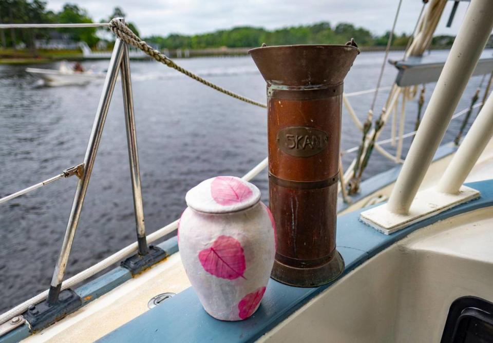 A biodegradable urn and a brass vessel used for the scattering of cremated remains line the rail of the “Enchantress” in Little River, S.C. Captain John Jaques uses his sailboat to take families to sea to help spread the cremated ashes of their loved ones. April 26, 2024.