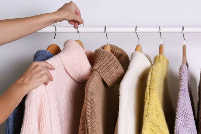 Woman choosing sweater on rack against white background, closeup