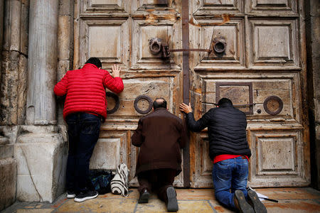 FILE PHOTO: Worshippers kneel and pray in front of the closed doors of the Church of the Holy Sepulchre in Jerusalem's Old City, February 25, 2018. REUTERS/Amir Cohen/File Photo