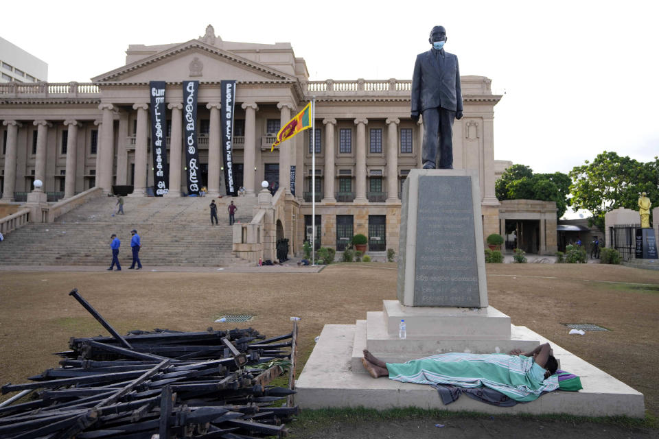 A protester sleeps under a statue in the compound of presidential secretariat in Colombo, Sri Lanka, Friday, July 15, 2022. Protesters retreated from government buildings Thursday in Sri Lanka, restoring a tenuous calm to the economically crippled country, and the embattled president at last emailed the resignation that demonstrators have sought for months.(AP Photo/Eranga Jayawardena)