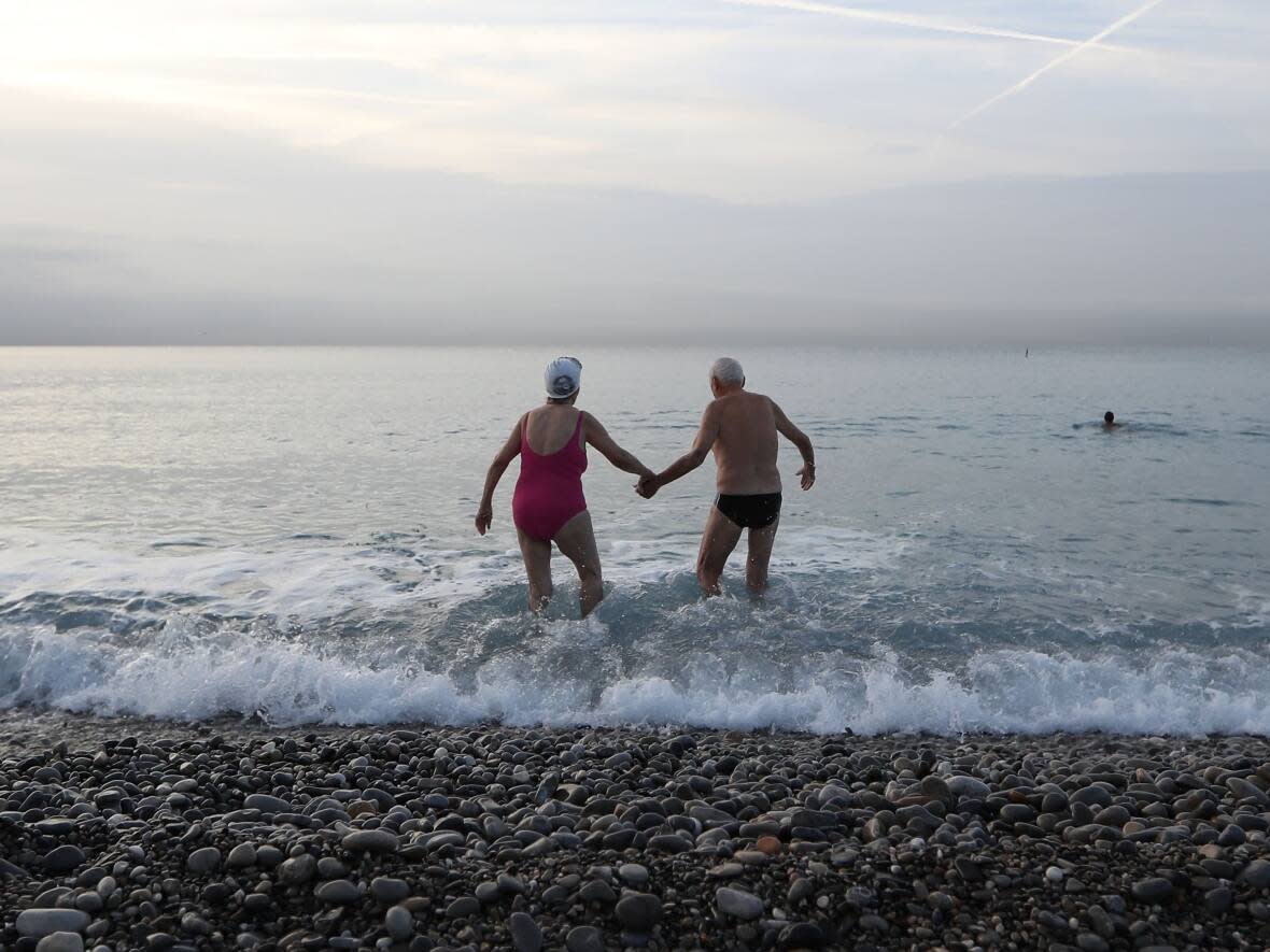 An elderly man and woman hold hands as they walk into the sea in this 2016 file photo. Canadians are getting fewer divorces, according to a new report. But they're also less likely to get married at all. (Valery Hache/AFP/Getty Images - image credit)