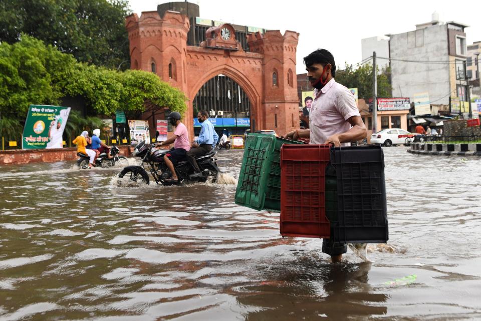 A man carrying crates wades along a water-logged street following heavy rains in Amritsar on July 19, 2020. (Photo by NARINDER NANU / AFP) (Photo by NARINDER NANU/AFP via Getty Images)