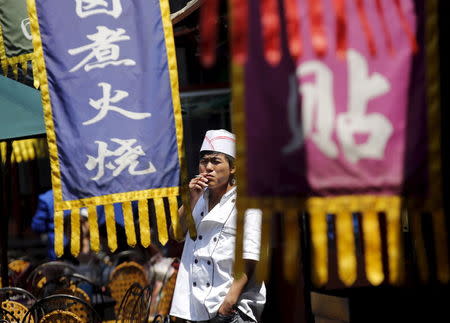 A cook smokes a cigarette behinds flags promoting restaurants during his break in Beijing, China, May 11, 2015. REUTERS/Kim Kyung-Hoon