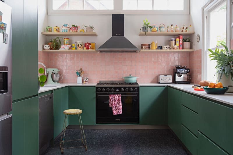 Pink tiles in kitchen with open shelves and green cabinets.