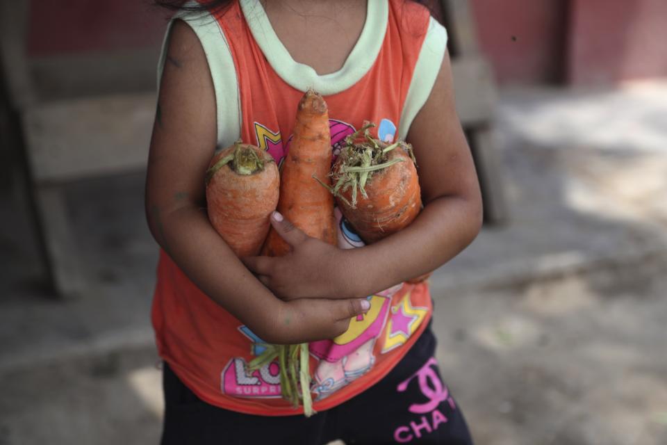 Una niña lleva zanahorias donadas a su madre, que está ayudando a preparar el almuerzo en un comedor de beneficencia en el barrio de chabolas de Villa María en Lima, Perú, el martes 2 de febrero de 2021, en medio de un segundo cierre completo de actividades mientras el país lucha contra un resurgimiento en los casos de COVID-19. La falta de ingresos estables ha obligado a muchas familias a depender de los comedores comunitarios en algunos de los barrios más pobres de la capital. (AP Foto/Martin Mejia)
