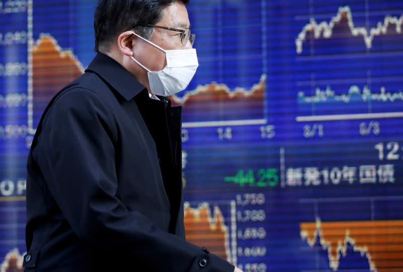 FILE PHOTO: A passerby wearing a protective face mask, following an outbreak of the coronavirus, walks past an electronic board showing the graphs of the recent movements of Japan's Nikkei share average outside a brokerage in Tokyo, Japan