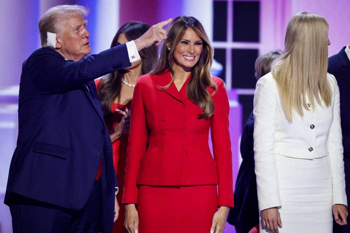 Donald Trump, Melania Trump and Ivanka Trump at an event. Melania is wearing a red suit and Ivanka is wearing a white suit.