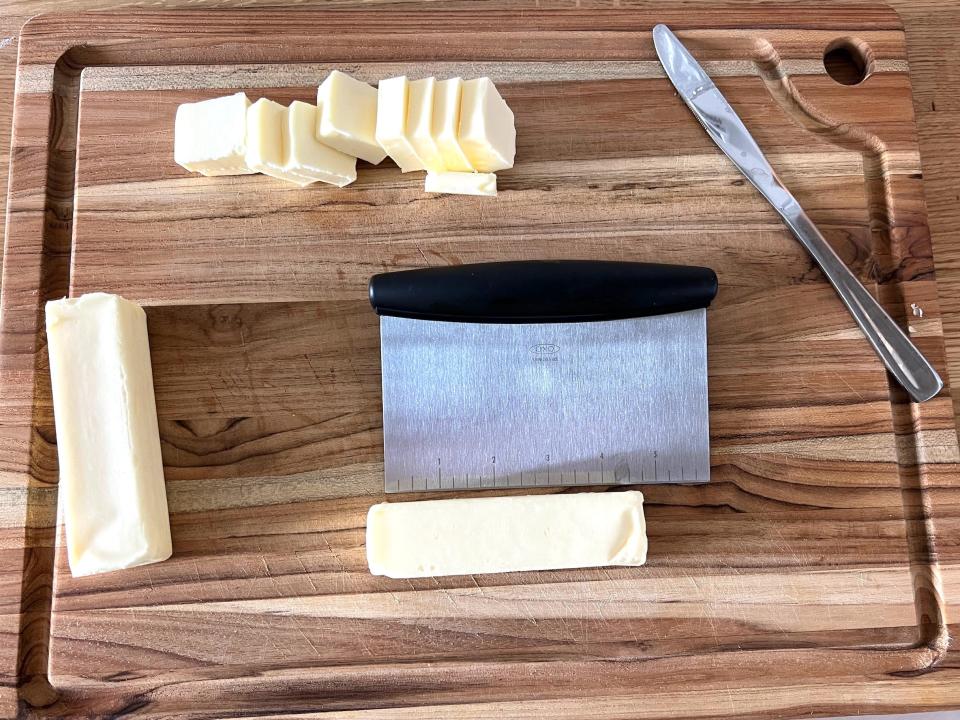 Butter being sliced into slices on a wood cutting board.