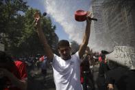 An anti-government protester raises his hands during clashes with police in Santiago, Chile, Tuesday, Oct. 22, 2019. The government said Tuesday that 15 people have died in five days of rioting, arson and violent clashes that were sparked by a hike in subway fares and have almost paralyzed the country. (AP Photo/Rodrigo Abd)