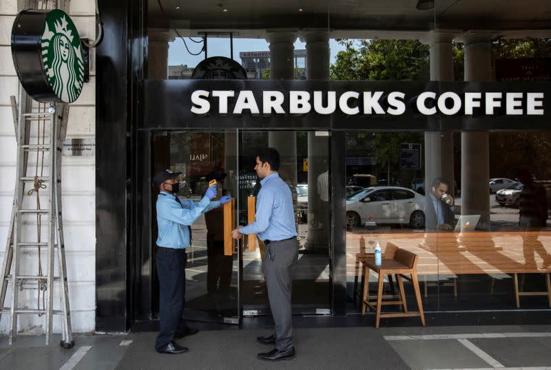 A private security guard checks the body temperature of a customer outside a Starbucks coffee shop, as a precaution against the spread of coronavirus, in New Delhi