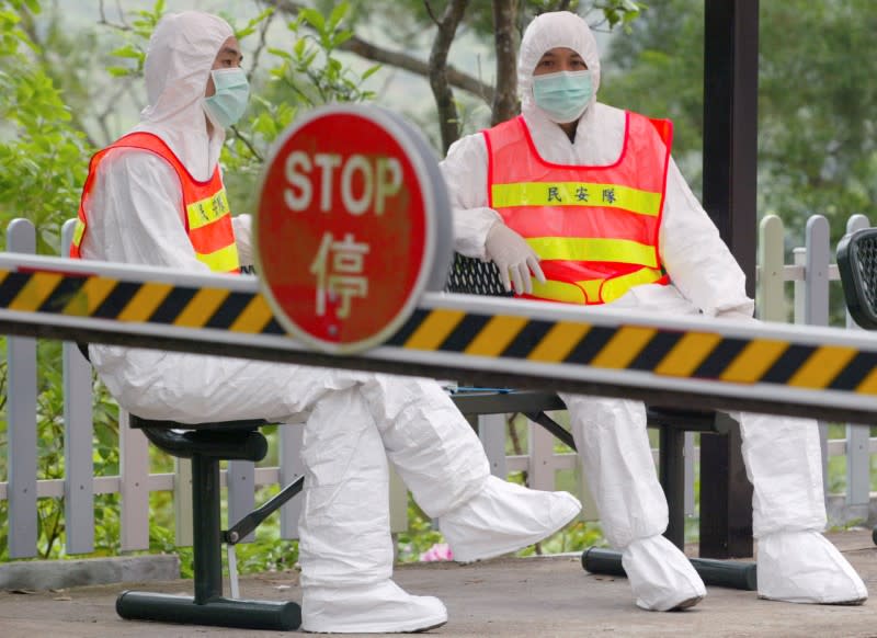 FOTO DE ARCHIVO: Oficiales de seguridad con trajes protectores y máscaras como medida preventiva contra el Síndrome Respiratorio Agudo y Grave (SARS), similar a la neumonía, se sientan a la entrada de un campo de aislamiento especial, donde unos 200 de los más de 400 residentes evacuados de Amoy Gardens, están siendo alojados en Hong Kong el 2 de abril de 2003