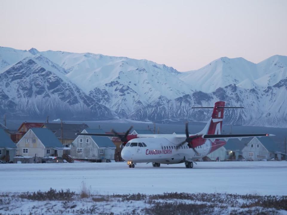 A Canadian North plane on the runway in Pond Inlet, Nunavut, with Bylot Island in the background. Changes to the airline's 2019 merger conditions now allow it to reduce services to communities to as little as one flight per week, and hike rates by up to 25 per cent per year. (David Gunn/CBC - image credit)