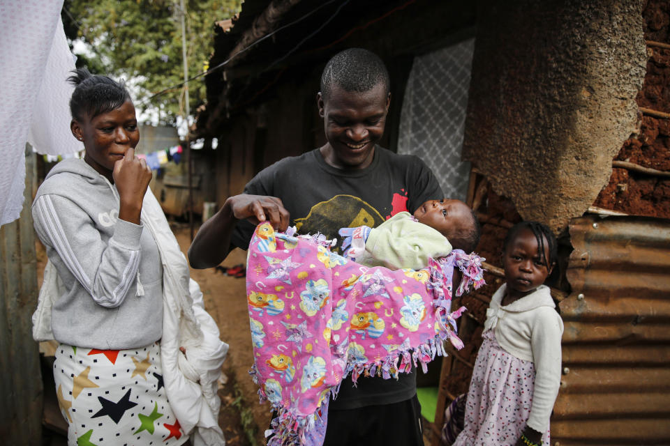 Mother Veronica Atieno, left, looks on as her husband Gabriel Owour Juma holds their daughter Shaniz Joy Juma, delivered a month earlier by a traditional birth attendant during a dusk-to-dawn curfew, accompanied by elder daughter Valine Shalom Juma, right, in the Kibera slum of Nairobi, Kenya Friday, July 3, 2020. Kenya already had one of the worst maternal mortality rates in the world, and though data are not yet available on the effects of the curfew aimed at curbing the spread of the coronavirus, experts believe the number of women and babies who die in childbirth has increased significantly since it was imposed mid-March. (AP Photo/Brian Inganga)