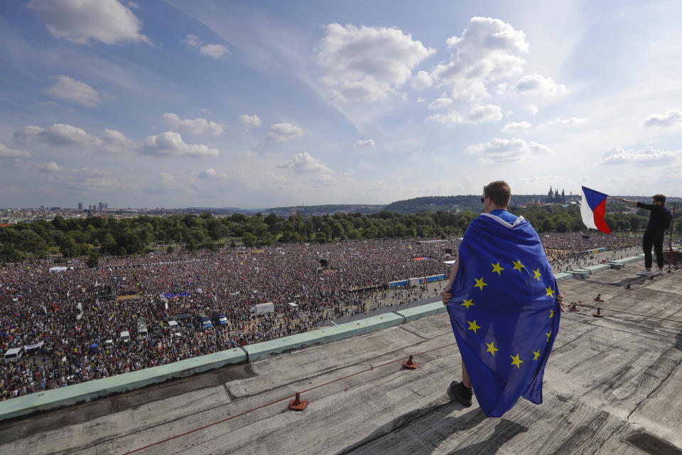 A man wrapped in in an European Union flag watches protesters gather in Prague, Czech Republic, Sunday, June 23, 2019. Protesters are on calling on Czech Prime Minister Andrej Babis to step down over fraud allegations and subsidies paid to his former companies. (AP Photo/Petr David Josek)